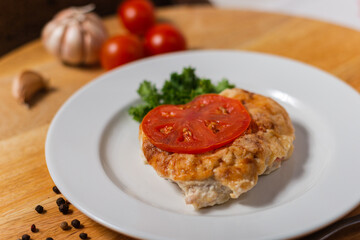 meat baked under a cheese crust with a tomato in a cafe on a white plate wooden background