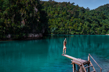 Fototapeta na wymiar Vacation and activity. Young woman in swimsuit enjoying blue tropical lagoon view standing on wooden springboard. Siargao Island, Philippines.