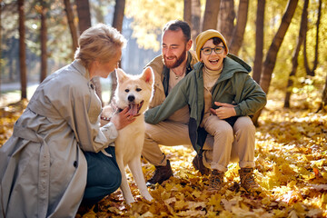excited family with dog on walk in autumn park. family, pet, domestic animal and people concept. young man, woman and child boy in coats outdoors on warm weather. human emotions concept