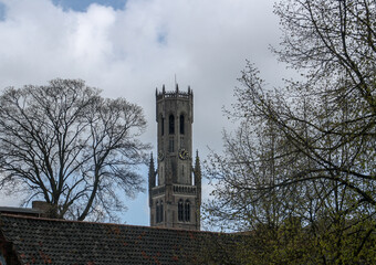 Parte superior del Campanario de Brujas entre árboles y tejados. La famosa torre en un hermoso cuadro entre las ramas sin hojas de unos árboles.
