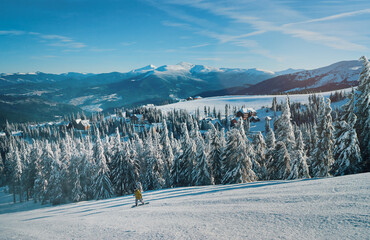 Snowy mountains and ski lifts. Skiers and snowboarders skiing downhill to village.