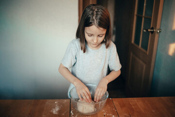 Fototapeta na wymiar A girl cooks a pie in the kitchen, isolation exercise for a child