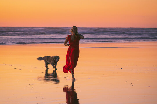 Female wearing a red dress running on the beach at sunset