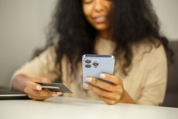 Woman buying online with credit card. Black female making a purchase in internet store with mobile phone and bank debit card. Person making money transfer online with smartphone app