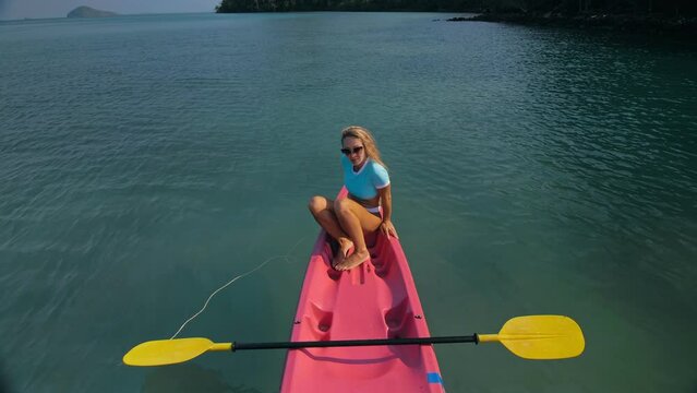 Pretty slim woman in elegant swimsuit lies in pink plastic kayak drifting on azure ocean at exotic resort upper view.