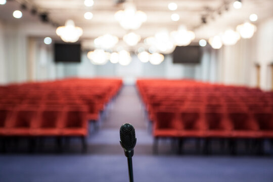 Interior Of A Conference Room. Microphone Detail Of The Speaker Facing The Room Full Of Red Chairs