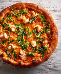 Pizza with shrimps and arugula isolated on light wooden background top view