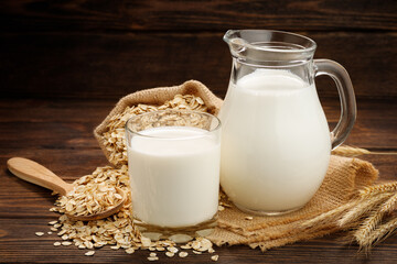 Oat flakes, jug and glass of milk on a wooden background.