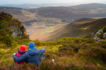 Fototapeta na wymiar Couple lovers from behind on the edge looking towards Lough Tay (Guinness Lake) in the wicklow mountains Ireland