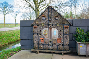 Wooden building with many small holes in the yard of a farm. Also known as an insect hotel.