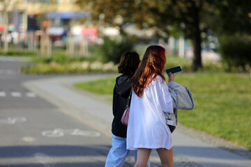 Dwie kobiety, dziewczyny z telefonem spacerują po chodniku, deptaku we Wrocławiu. 
