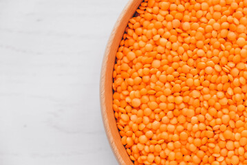 Raw red lentils in a wooden bowl on a white table