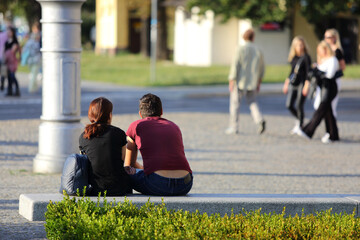Para młodych ludzie wypoczywają, siedzą na betonowej ławce we Wrocławiu w cenrum miasta. 
