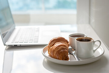 Morning coffee, croissant and laptop near the window