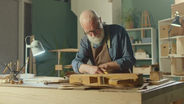 Professional Elderly Man Carpenter Working on Wood Using Carpentry Tools in the Garage. Craft Authentic Workshop. Handicraft, Creative Small Business. Profession, Art and Hobby Concept.