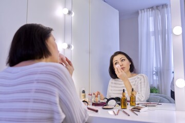 Beautiful middle aged woman doing makeup in front of a mirror.