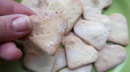 Hand holding warm heart shaped cookies on green plate background