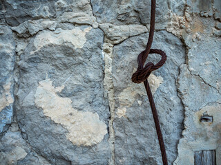 imagen detalle de pared de piedra con juntas de cemento y una cuerda de acero con un nudo llena de oxido 