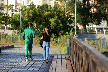 Para młodych ludzie spaceruje deptakiem, chodnikiem w parku, drewniany most, Wrocław. 
