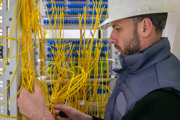 Portrait of an engineer working in the server room of the data center. A man lays fiber optic wires...