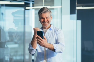 Successful businessman, in a shirt for the sake of success, holding a phone in his hands, working in a modern office