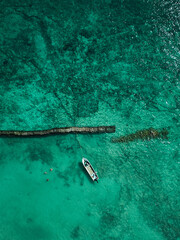 White boat with people on blue water from a bird's eye view. People next to the boat are snorkelling.
