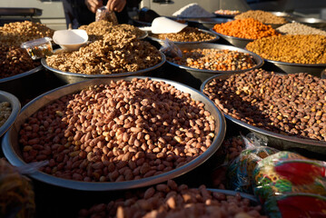 Close up of stainless steel scoop with roasted piled peanuts on display at street market. Peanuts in plastic bag ready for sale. High quality photo