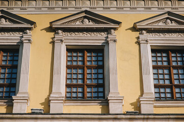 Obraz premium Three windows on the facade of a house with beige plaster in the central historical part of the city. Beautiful decorative architecture with reliefs, cornice and white columns in Lviv, Ukraine.
