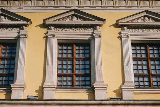 Three windows on the facade of a house with beige plaster in the central historical part of the city. Beautiful decorative architecture with reliefs, cornice and white columns in Lviv, Ukraine.