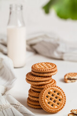 Fototapeta na wymiar Stack of crispy cookies with chocolate cream and bootle of milk on a white table.