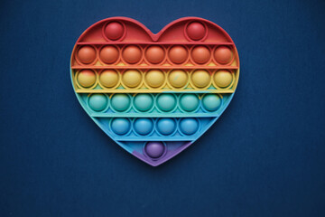 Close-up. Heart, silicone colorful anti-stress toy on a blue background. Click the pop up bubble. simple toy with dimples. The concept of romance, love, gift, valentine's day, holiday.