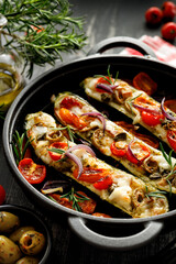 Baked zucchini stuffed with goat cheese and vegetables, sprinkled with herbs in a cast iron baking dish, close up view