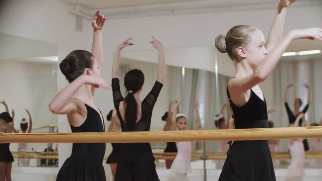 Group of little girls training ballet in the mirror studio with a trainer