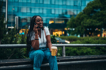 African american woman using smartphone and drinking coffee takeaway