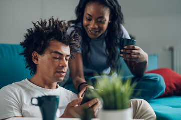 African american couple using smartphone while drinking coffee at home