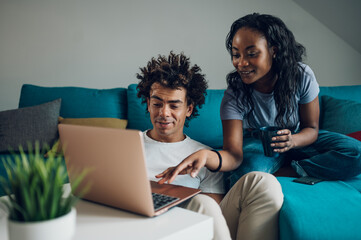 African american couple relaxing on couch with laptop and coffee at home
