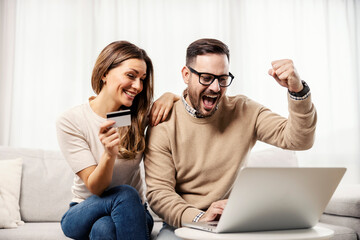 A happy couple at their home shopping online on the laptop.