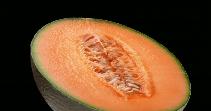 One half of a cantaloupe melon is rotating. Isolated on black background.