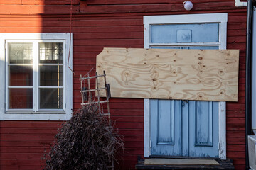 Door boarded up with plywood in a derelict wooden house. Red painted walls and blue door.