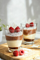 Three-layer mousse dessert made of chocolate and vanilla, decorated with fresh raspberries and coconut flakes in glasses on the table. Brunch, dessert for lovers