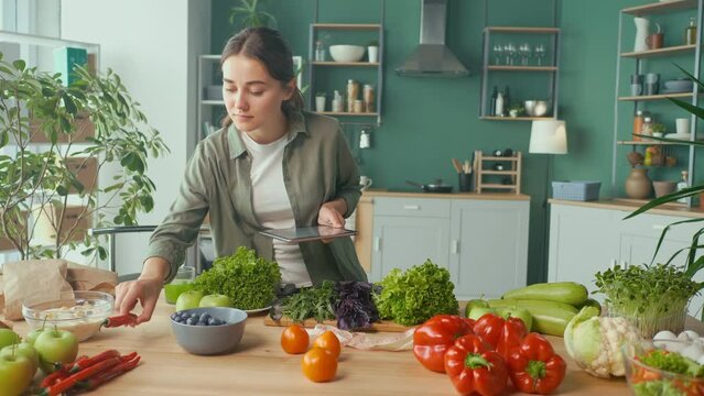 Young Woman Makes a Diet Plan of Correct Nutrition Using a Tablet in the Kitchen, Using a Calorie Counter in a Weight Loss App. Nutrition and Dietetics. Healthy Food and Technology Concept.