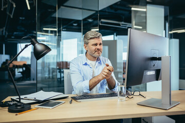 Senior and experienced businessman, looks frustrated at the monitor, complains about poor performance, man at work