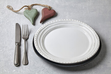 An empty white plate with cutlery and two decorative wooden hearts