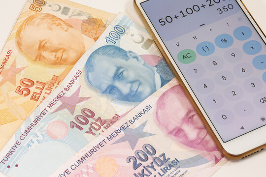 50, 100 and 200 turkish banknotes and calculator app open mobile phone on isolated background. Banknotes in selective focus. Time is money concept.