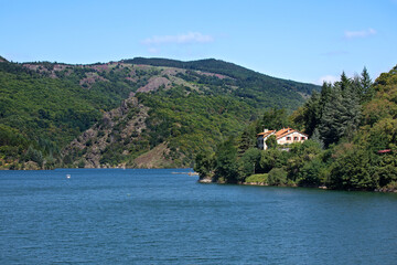 Fototapeta na wymiar Lac d'altitude au-dessus d'un barrage avec hôtel restaurant de tourisme pour des vacances en été en montagne dans les Cévennes en France.