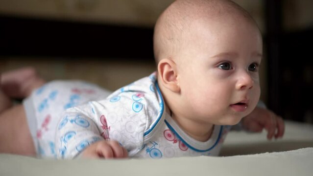 Newborn Active Baby Cute Smiling Teethless Face Portrait Early Days On Stomach Developing Neck Control. 5 Months Child On White Bed Looking on Camera. Infant, Childbirth, Parenthood, Beginning Concept