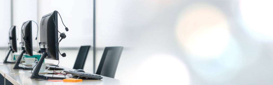 Call center computers and headsets all in office in widen view. Telemarketing, customer support agent provide service on telephone video conference call.