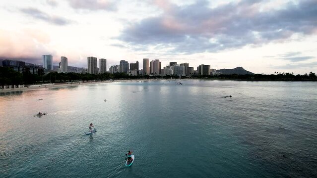 Sunset aerial view of Ala Moana Beach with paddle boarders and swimmers with Diamond Head and Waikiki skyline in the background