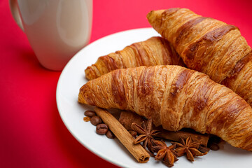 Fresh French breakfast concept with out-of-oven croissants on a white plate, a blurred cup of tea or coffee on background