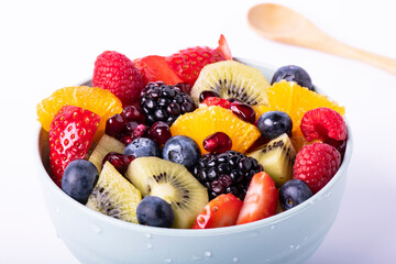 Fresh mixed fruit salad in a bowl with a wooden spoon in the foreground. White background